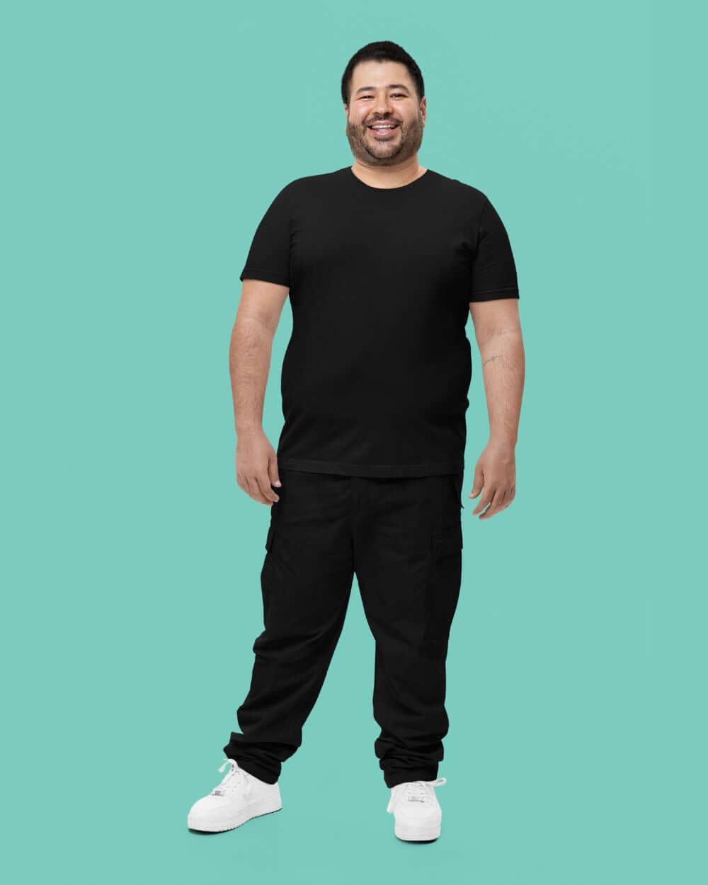 Man smiling in a black crewneck t-shirt and black pants against a mint green background.